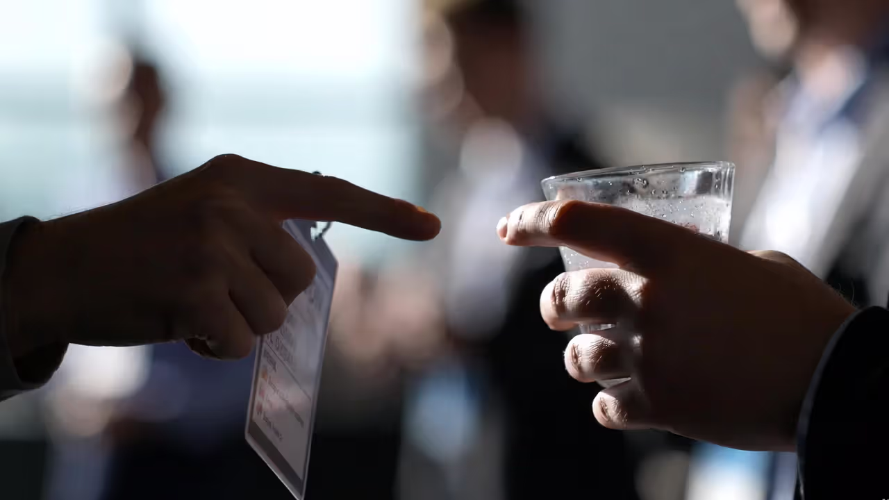 Close-up of hands holding a badge and drink with blurred conference crowd