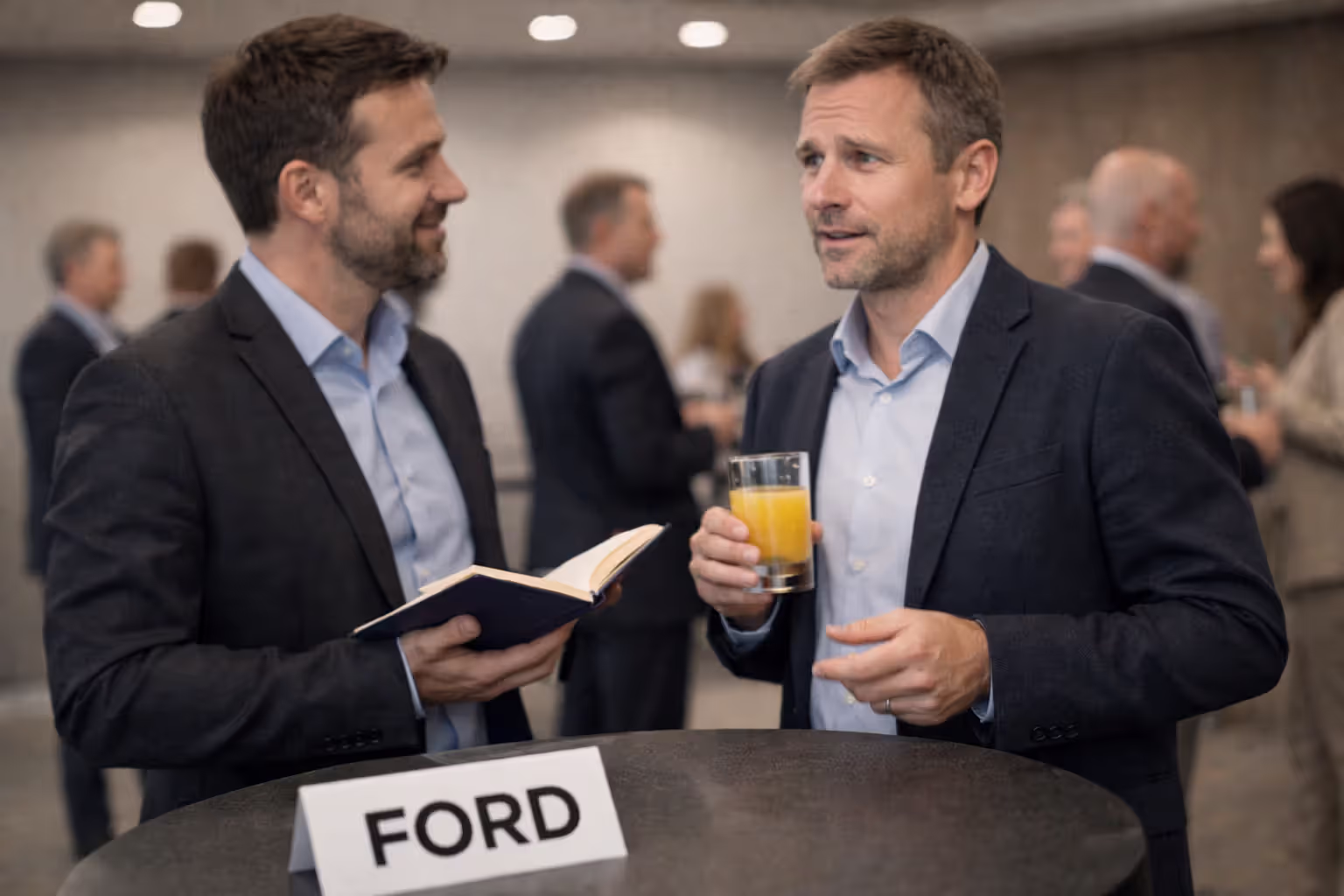 Two professionals talking at event with a note card labeled “FORD” on table